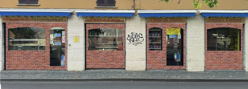 La facciata di Panfruit in via Torriani 12: quattro vetrine con le tende blu e le insegne Panfruit Minimarket, Pane e Pizza, Dolci da Forno, Frutta e Verdura