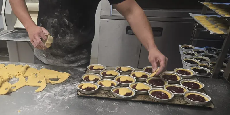 Mani che preparano le crostatine a cuore sul banco del laboratorio
