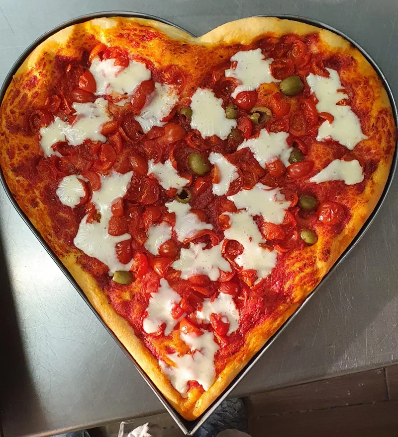 Pizza a forma di cuore con pomodorini, mozzarella e olive verdi, nella sua teglia