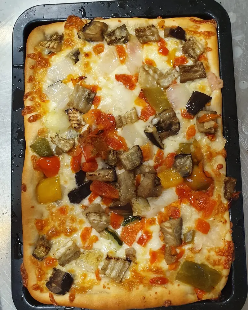 Teglia di pizza con verdure, pomodorini e mozzarella appena sfornata