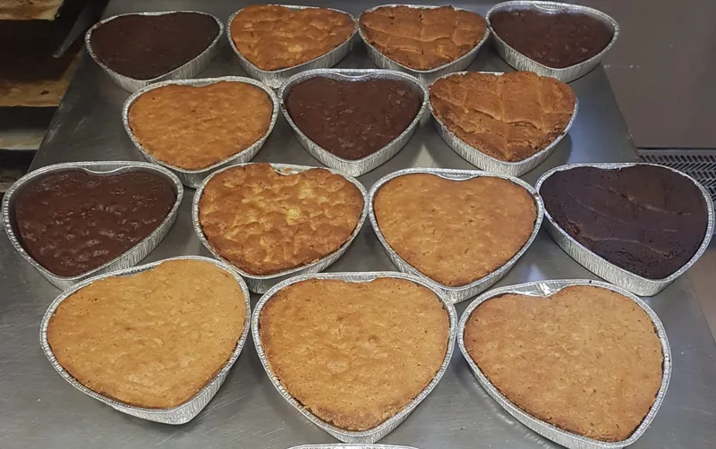 Torte da forno a forma di cuore, chiare e al cacao, nelle vaschette sul banco del laboratorio